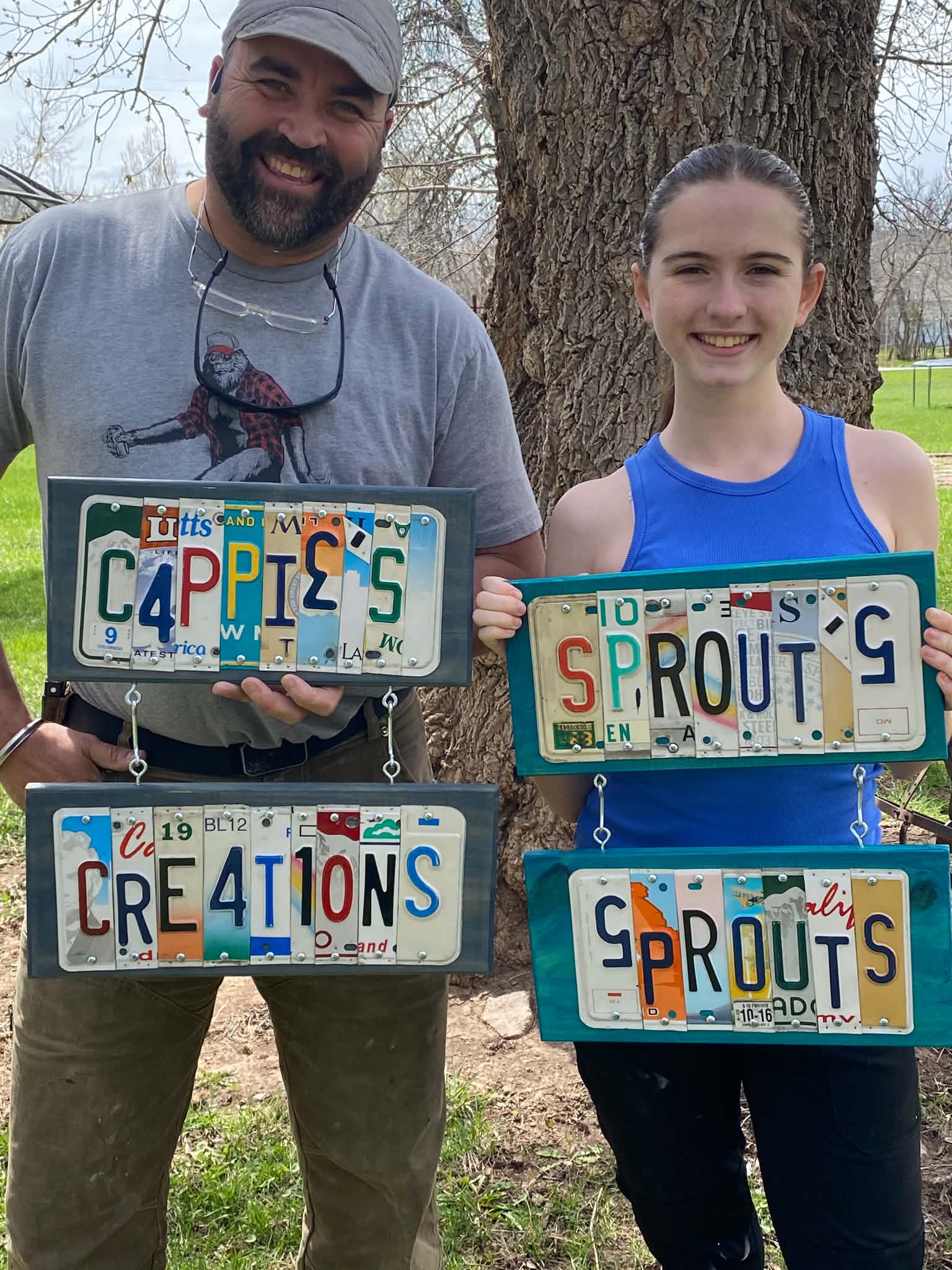Happy customers holding Cappies Sprouts and Creations custom license plate signs
